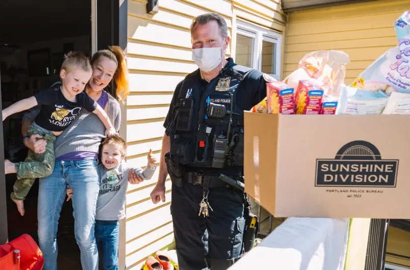 A Portland Police Officer Delivers a Food Box from Sunshine Division to a Mother and Her Two Boys