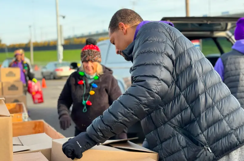 A Sunshine Division Volunteer Helps Pack Food Boxes into a Car