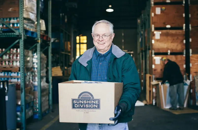 Sunshine Division Volunteer Holding Food Box in Warehouse